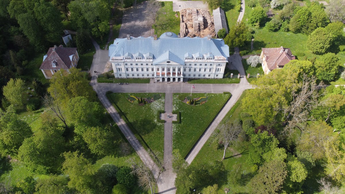 Vēsturiska Latvijas muiža Kazdangā no putna lidojuma — klasisks muižas komplekss zaļā dabas apkārtnē